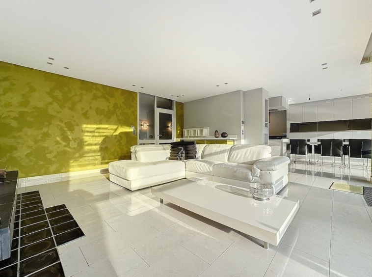 Salon moderne lumineux avec canapé blanc, mur vert texturé et espace ouvert convivial.