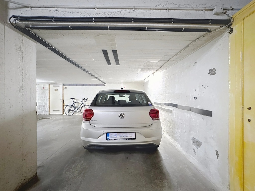 Voiture Volkswagen blanche dans un garage urbain moderne avec porte jaune et rack à vélos.