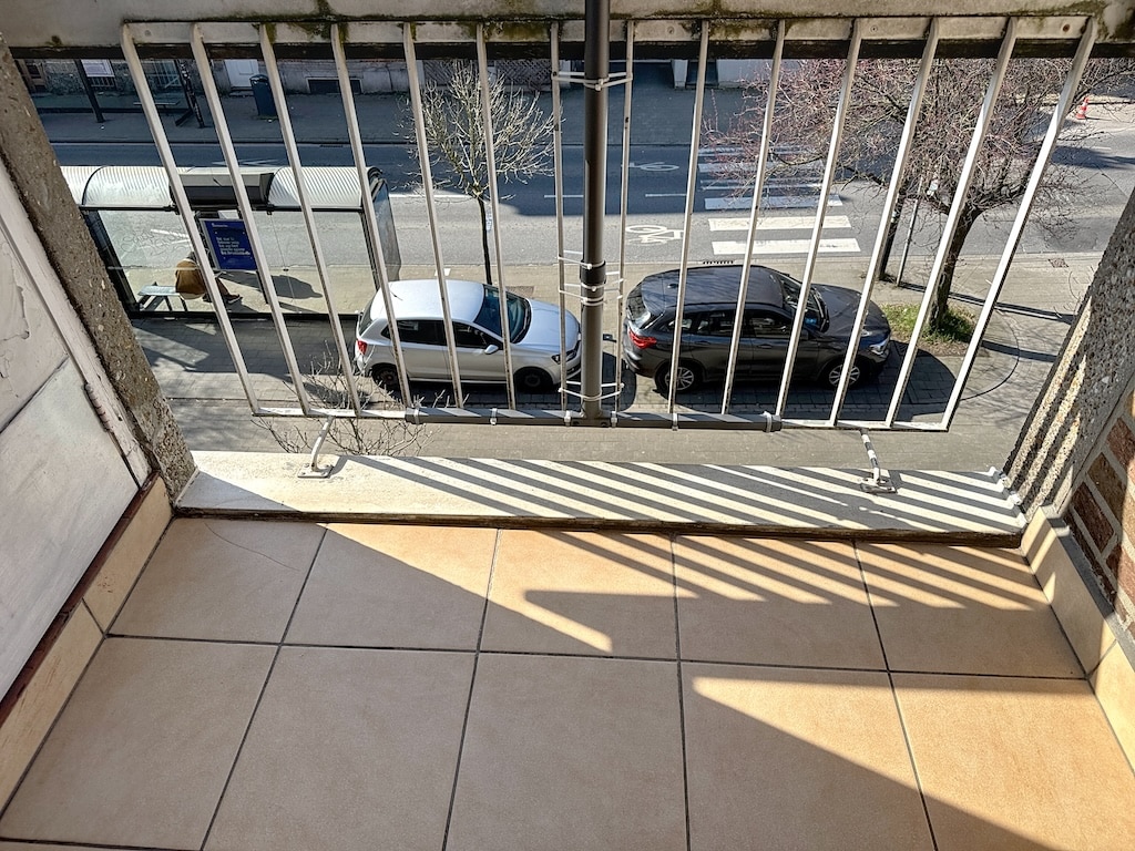 Balcon urbain avec vue sur rue, voitures, arbres et arrêt de bus ensoleillé.