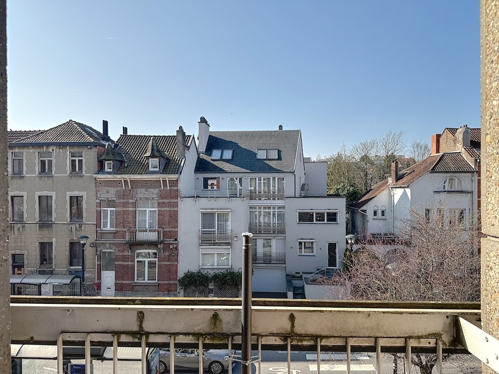Balcon sur un quartier mixte historique et moderne, avec jardins, arbres et ciel ensoleillé.