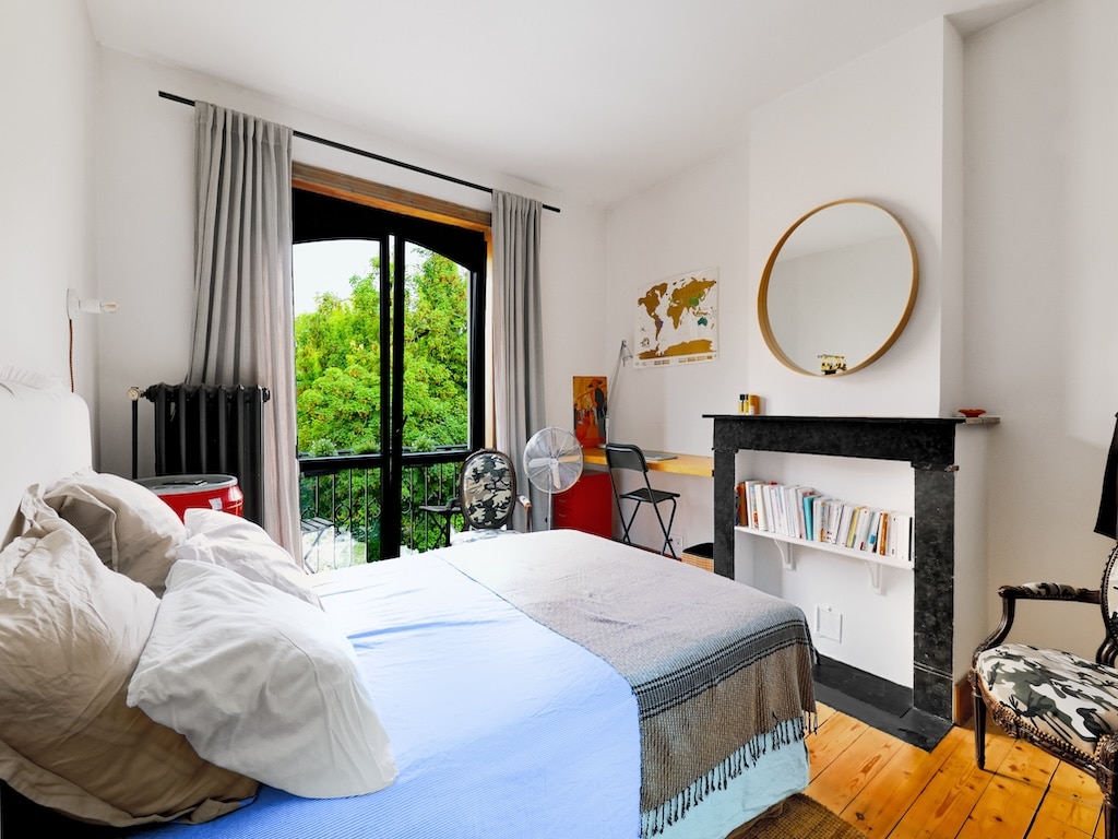 Chambre lumineuse avec vue verte, lit doux, espace de travail cosy, parquet chaleureux, style moderne et intime.
