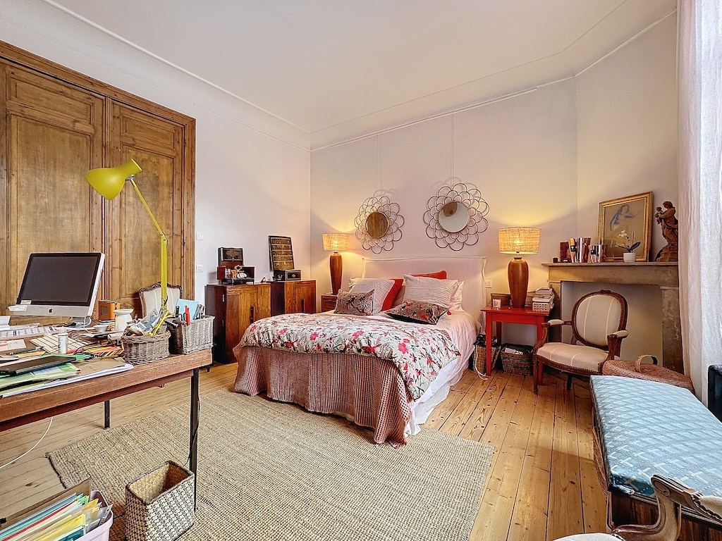Chambre chaleureuse avec mobilier en bois, lit floral, miroirs ronds et coin bureau accueillant.