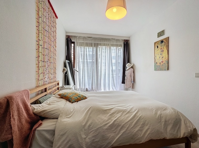 Chambre lumineuse, cosy et colorée avec lit blanc, miroir en bois et œuvres d’art murales.