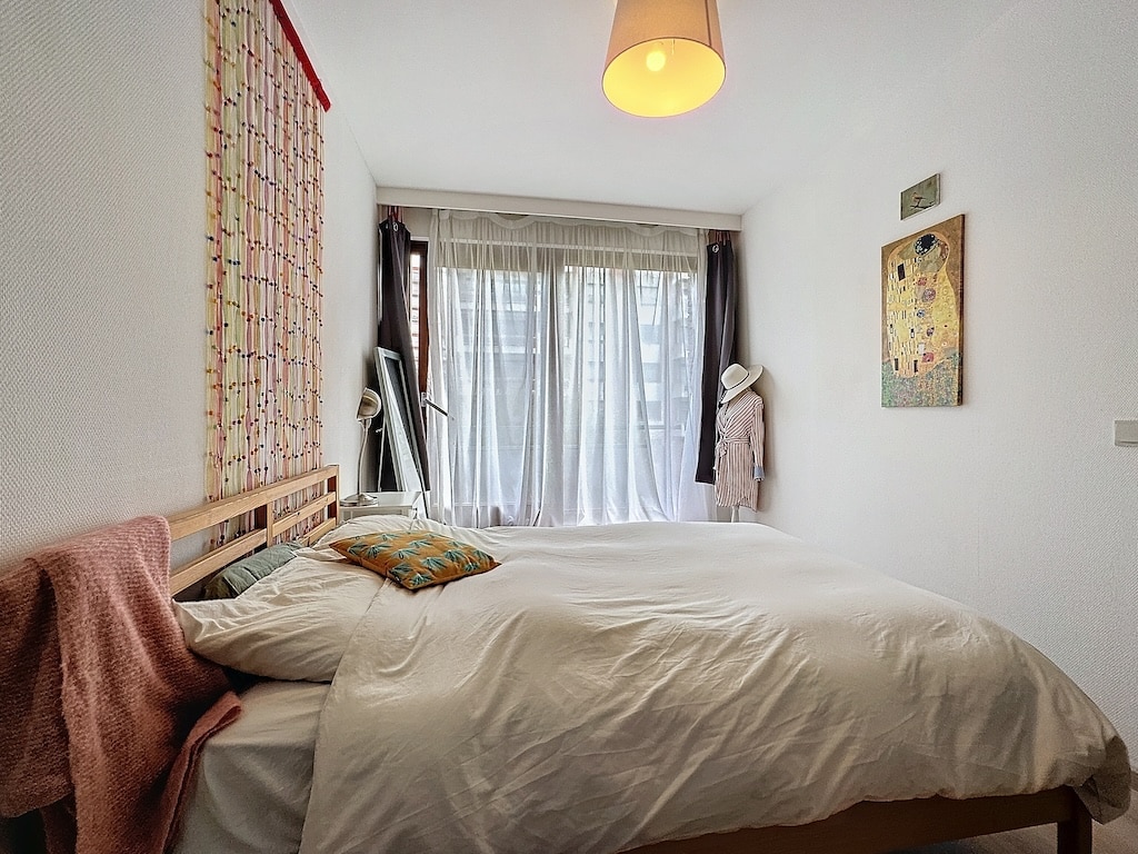 Chambre lumineuse, cosy et colorée avec lit blanc, miroir en bois et œuvres d’art murales.