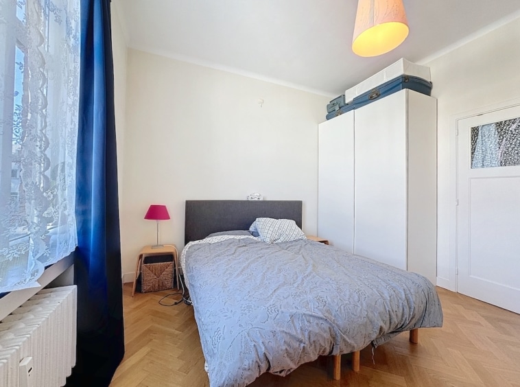 Chambre lumineuse minimaliste avec lit, grande fenêtre, placard blanc et touche de couleur rose.
