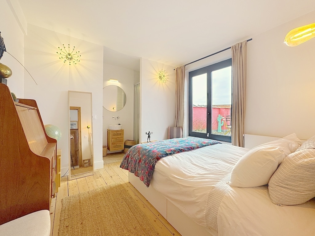 Chambre lumineuse et moderne avec décoration minimaliste, lit blanc, lampes rétro, grand miroir et fenêtres beige.