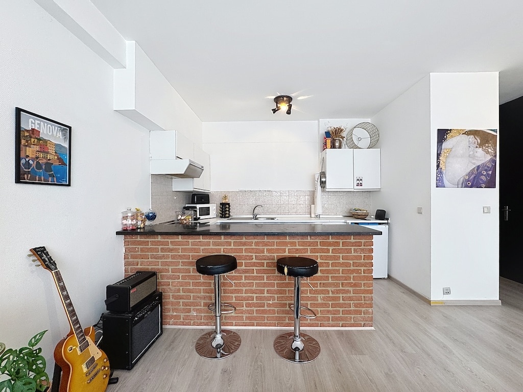 Cuisine moderne ouverte avec bar en pierre noire, ambiance chaleureuse et touches musicales.