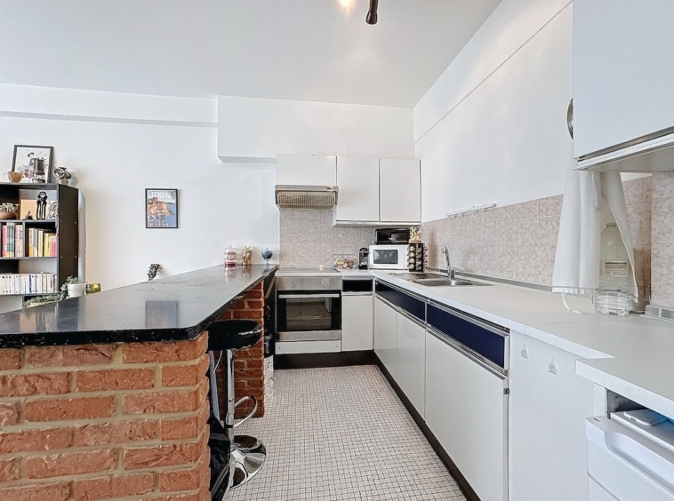 Cuisine moderne avec îlot, murs blancs, meubles laqués, touches de bleu marine, sol mosaïque élégante.