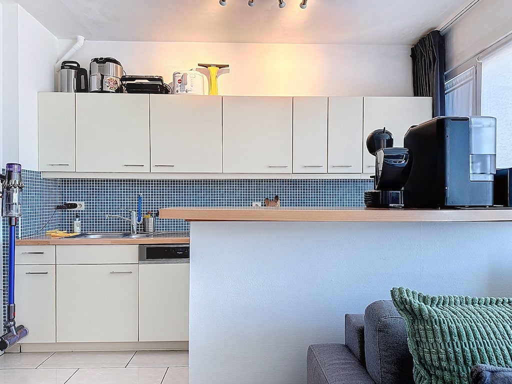 Cuisine contemporaine compacte avec dosseret bleu, électroménagers élégants et espace salon cosy.