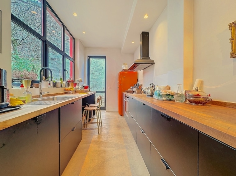 Cuisine contemporaine avec mobilier noir, plans en bois, luminosité naturelle, frigo rouge, plantes déco.