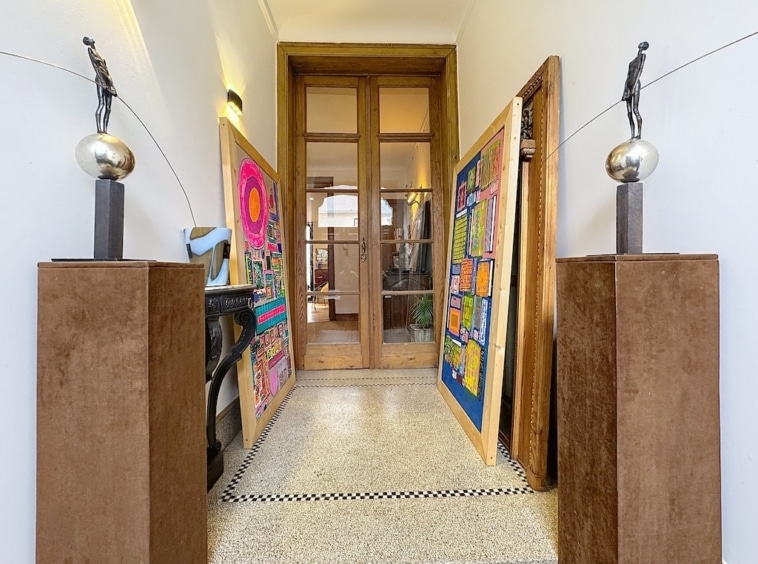 Hall dentrée artistique avec sculptures, œuvres colorées, portes en bois et sol en mosaïque élégante.