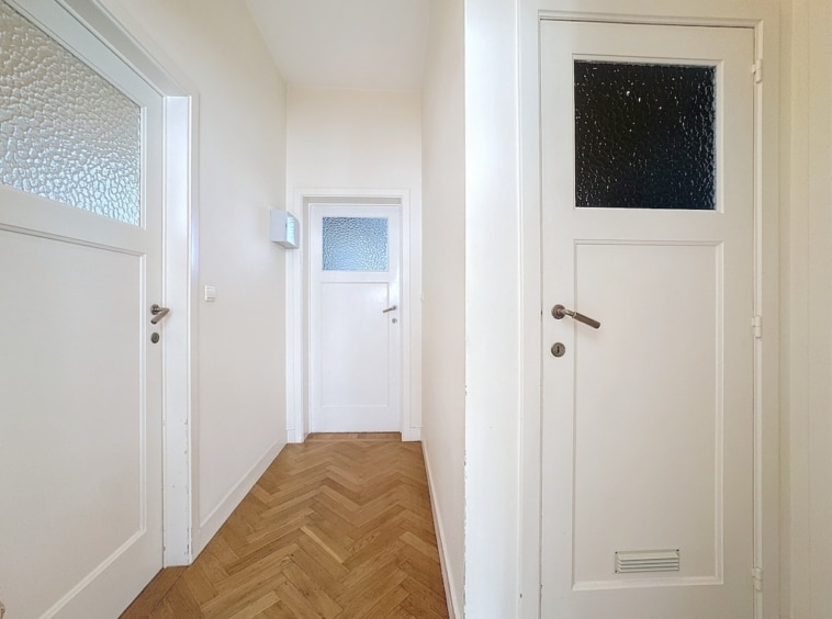 Hall minimaliste lumineux avec murs crème, sols en chevrons et portes en verre élégantes.