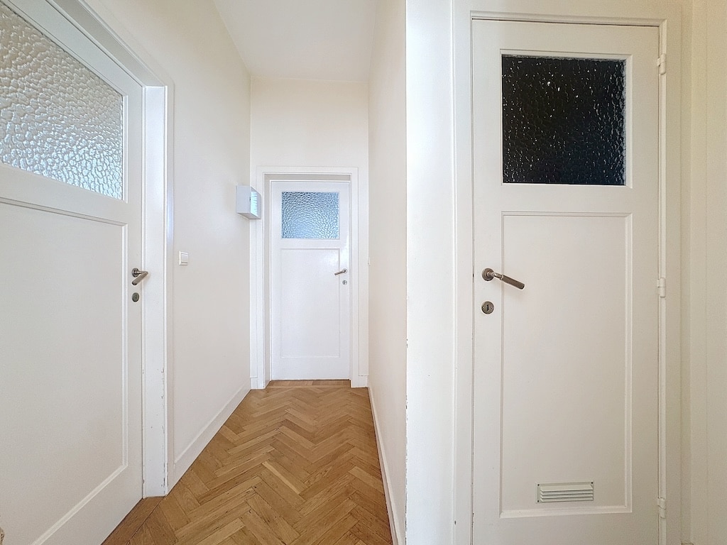 Hall minimaliste lumineux avec murs crème, sols en chevrons et portes en verre élégantes.