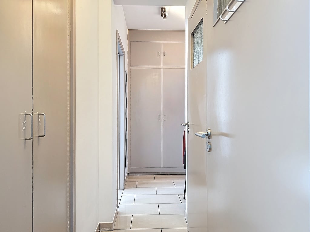 Couloir lumineux minimaliste avec portes métalliques, grande porte vitrée et sol en carreaux clairs.