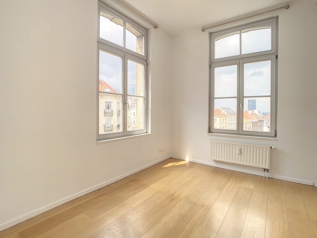 Espace minimaliste lumineux avec vue urbaine, murs blancs, bois clair, et radiateur discret.