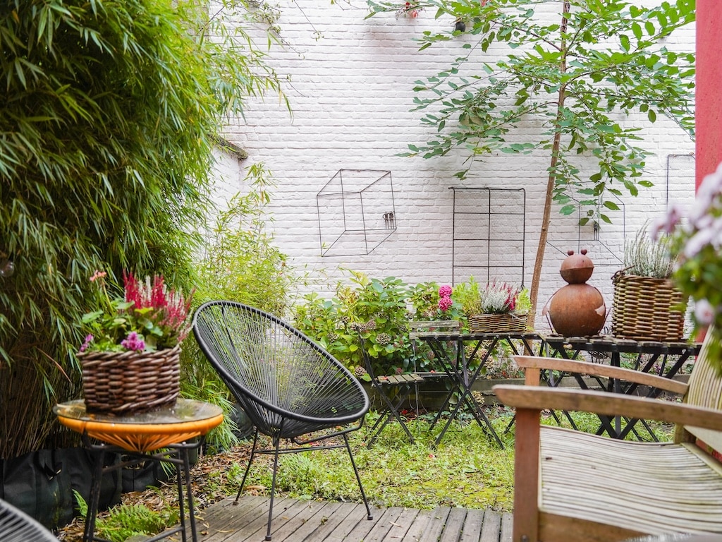 Jardin serein avec fleurs colorées, mobilier en bois et chaise Acapulco pour la détente extérieure.