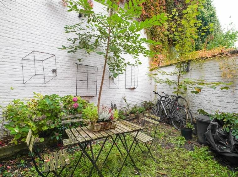 Jardin urbain charmant avec fleurs colorées, vélos, mobilier métallique et plantes grimpantes.