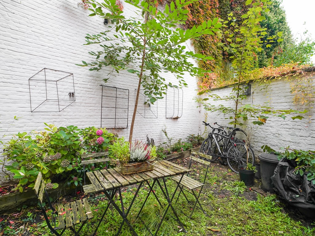 Jardin urbain charmant avec fleurs colorées, vélos, mobilier métallique et plantes grimpantes.