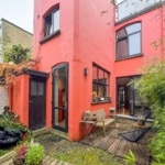 Maison moderne colorée avec terrasse en bois et jardin zen luxuriant.