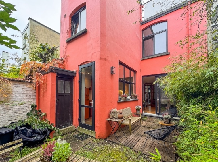 Maison moderne colorée avec terrasse en bois et jardin zen luxuriant.