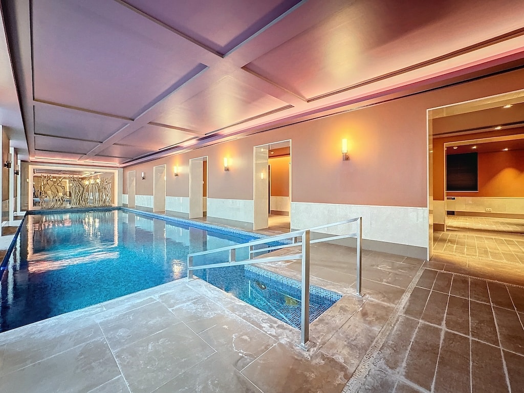 Piscine intérieure luxueuse avec eau bleue, murs pêche douce, éclairage subtil et décor élégant.