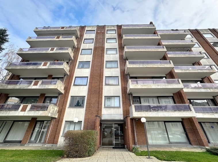 Appartement urbain moderne avec balcons en béton, briques rouges et grandes fenêtres lumineuses.