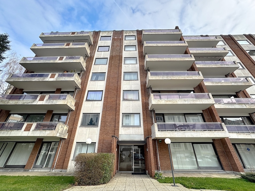 Appartement urbain moderne avec balcons en béton, briques rouges et grandes fenêtres lumineuses.