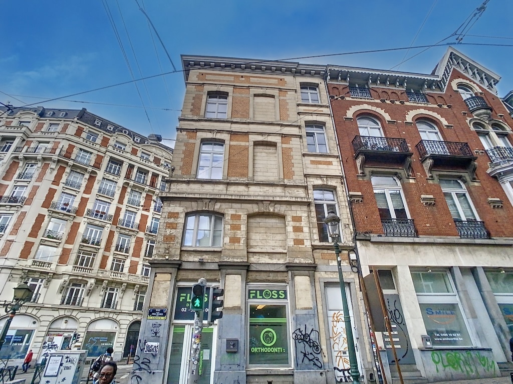 Rue urbaine animée avec bâtiments historiques, modernité et vie quotidienne sous ciel ensoleillé.
