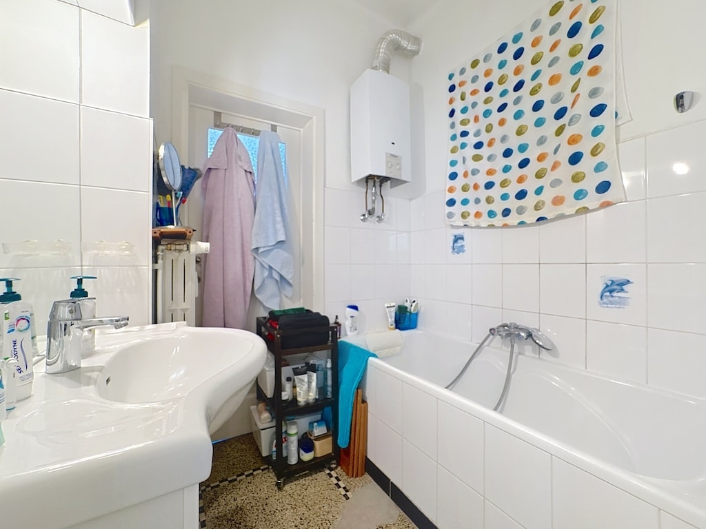 Salle de bain lumineuse compacte avec douche, lavabo moderne et rangement pratique en blanc.