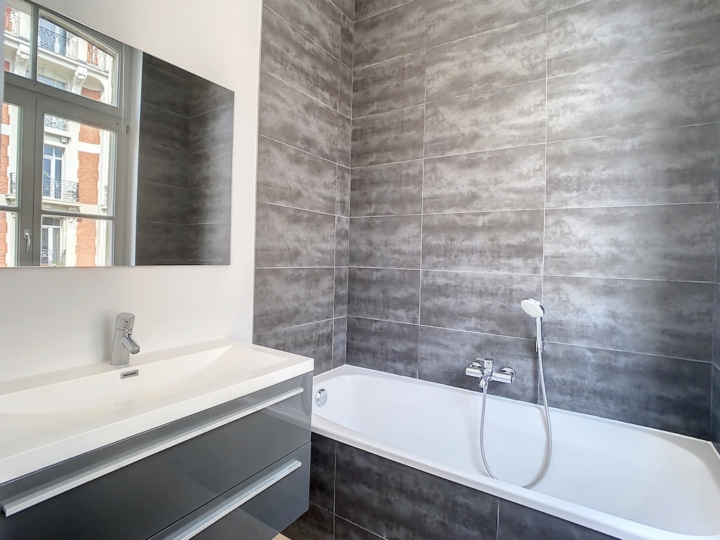 Salle de bain moderne avec baignoire blanche, miroir grand format et design épuré.