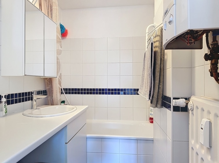 Salle de bain moderne avec carrelage blanc, bande bleue, baignoire, lavabo, miroirs et chauffage.