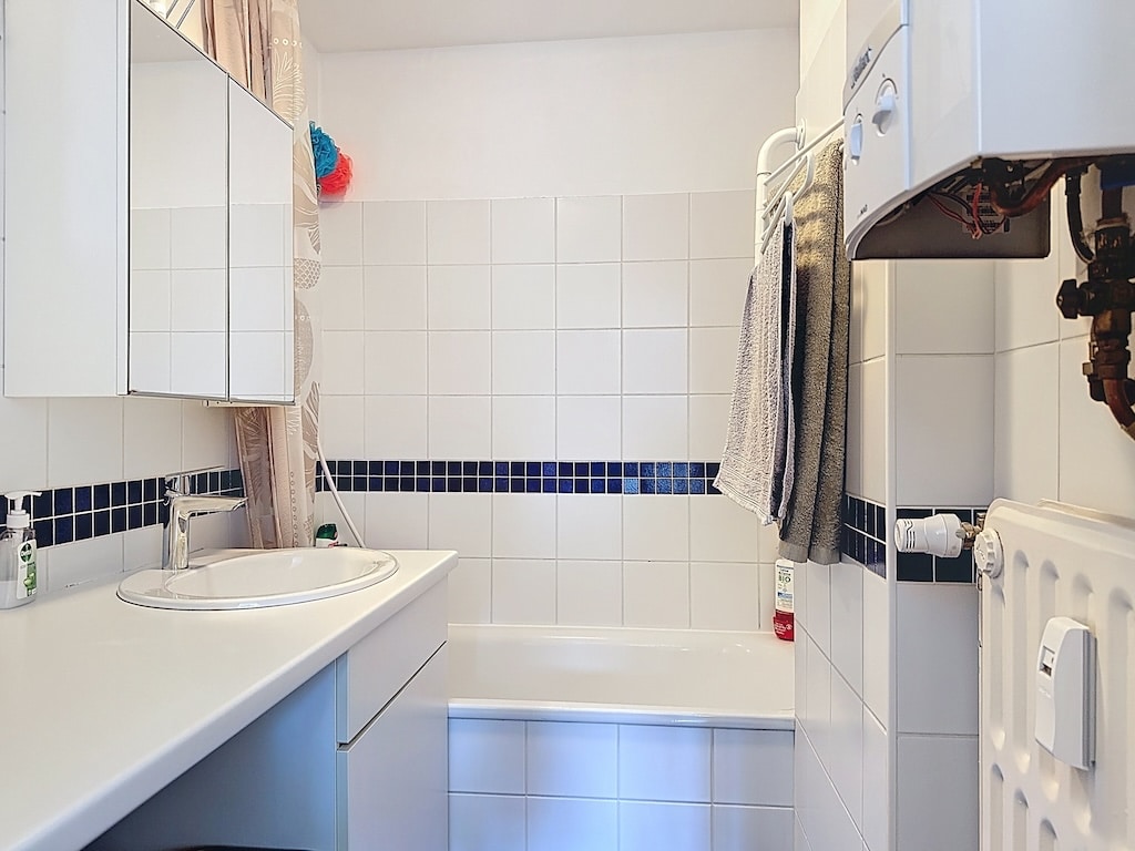 Salle de bain moderne avec carrelage blanc, bande bleue, baignoire, lavabo, miroirs et chauffage.