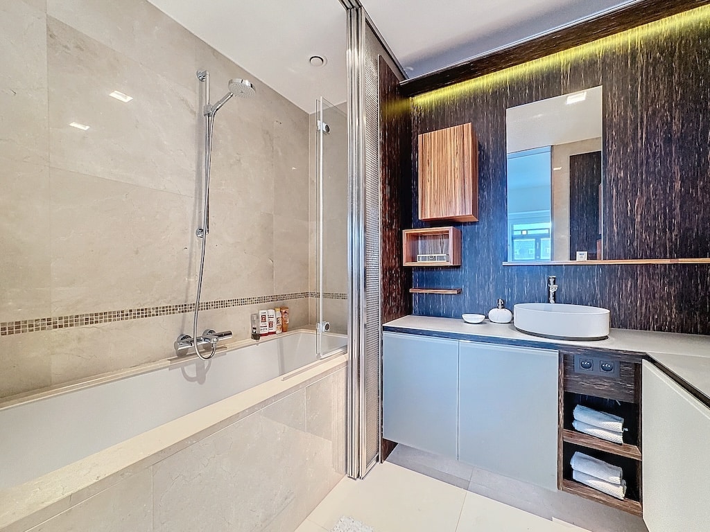Salle de bain élégante avec baignoire, meuble en bois, éclairage chaleureux, ambiance zen.