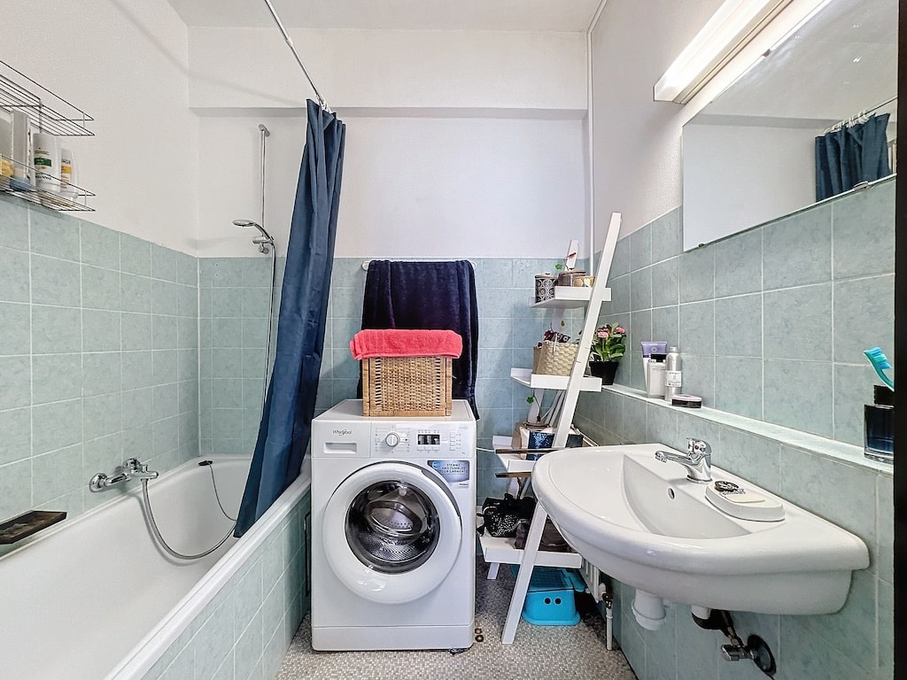 Salle de bain compacte avec baignoire, lave-linge, lavabo et plantes pour un espace pratique et lumineux.