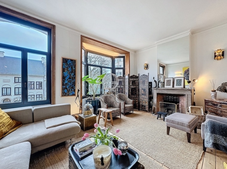 Salon élégant avec lumière naturelle, canapé gris, cheminée classique et décor artistique chaleureux.