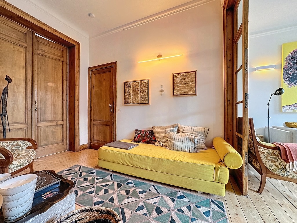 Salon moderne avec canapé jaune, décoration chaleureuse, œuvres earthy et lumière naturelle.