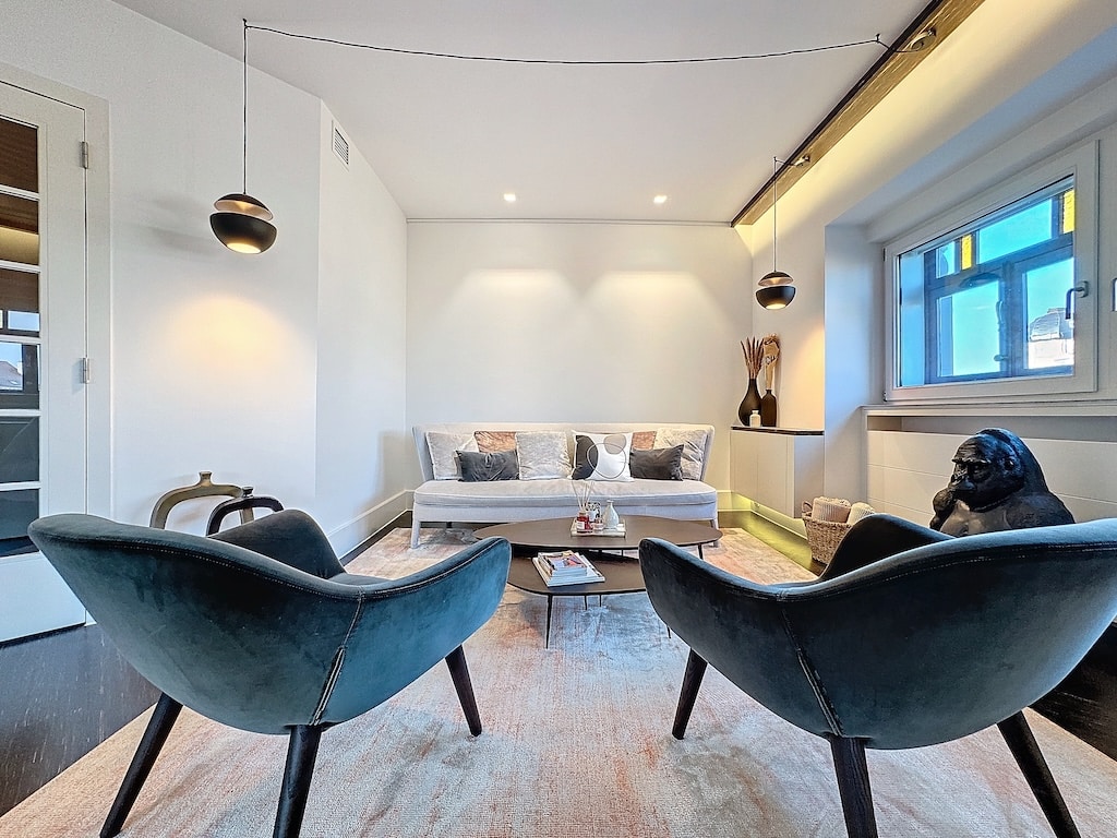 Salon moderne lumineux avec canapé, fauteuils teal, éclairage doux et décoration artistique élégante.