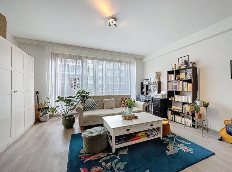 Salon lumineux moderne avec mobilier beige, plantes fraîches et décoration élégante.