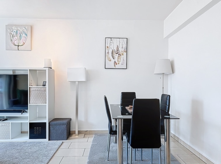 Salon moderne avec table en verre, mobilier noir, éclairage chaleureux, déco minimaliste élégante.