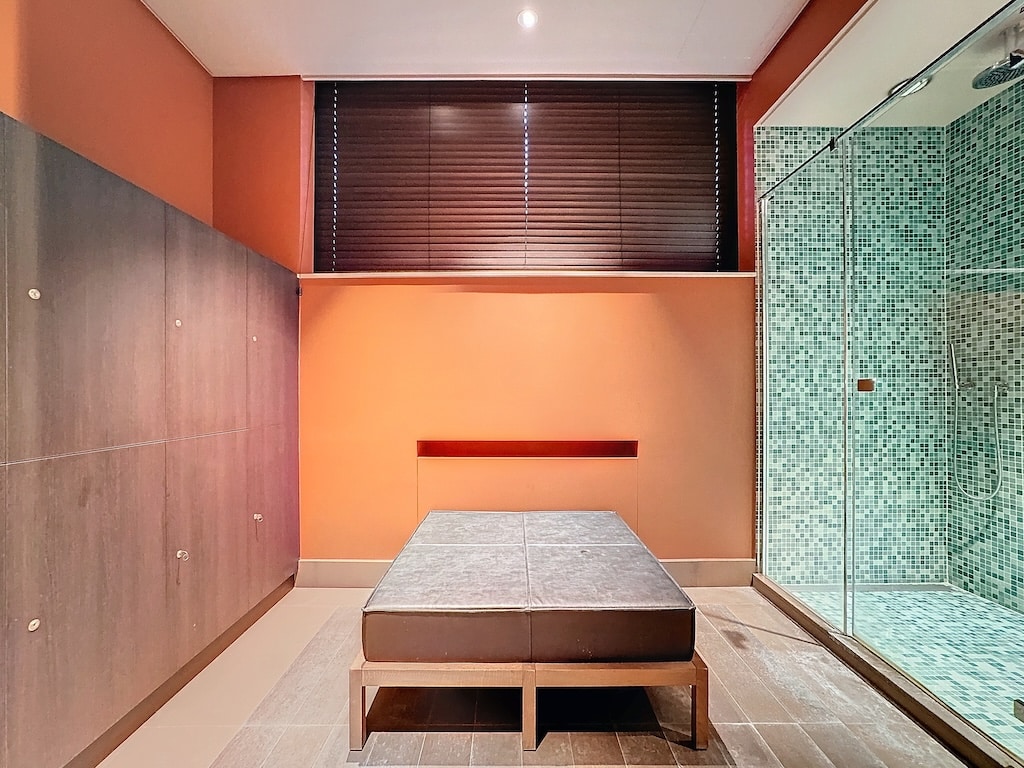 Spa moderne avec douche mosaïque verte, banc gris et décoration chaleureuse en bois et orange.