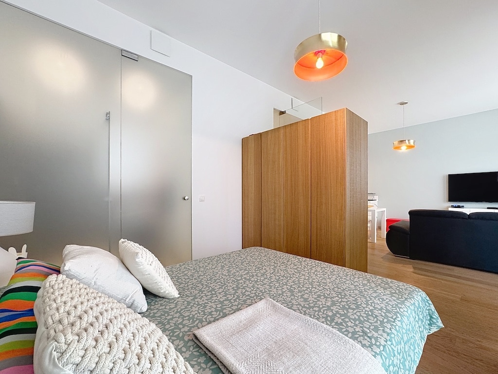 Chambre moderne lumineuse avec mobilier en bois, éclairage cuivre, ouverte sur le salon lumineux.