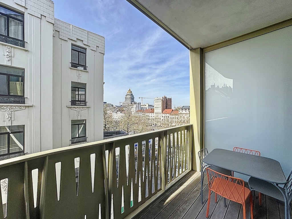 Balcon urbain lumineux avec mobilier moderne, vue panoramique sur la ville et bâtiment emblématique.