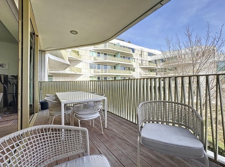 Balcon moderne avec mobilier en rotin, vue urbaine, sol en bois et ambiance lumineuse.