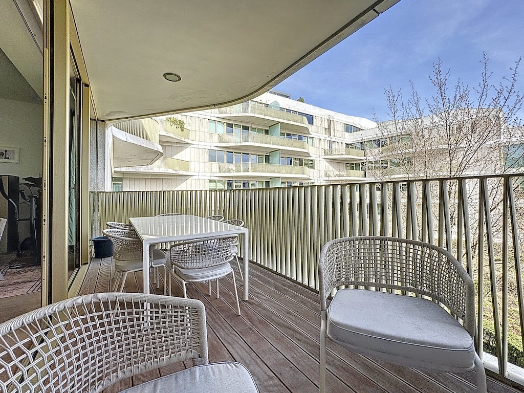 Balcon moderne avec mobilier en rotin, vue urbaine, sol en bois et ambiance lumineuse.