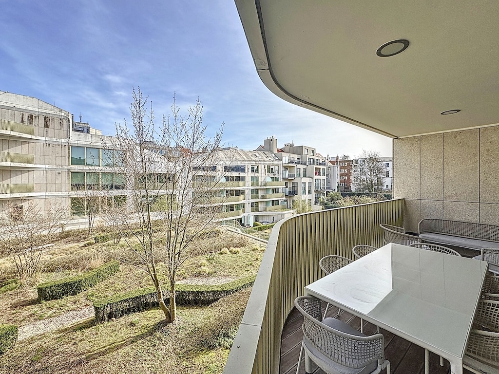 Balcon moderne avec mobilier blanc, vue panoramique sur nature et architecture urbaine.