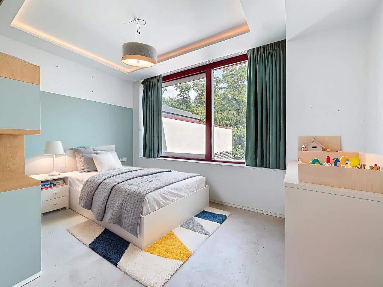 Chambre minimaliste moderne avec espace enfant coloré, lit gris, murs pastel et déco géométrique.