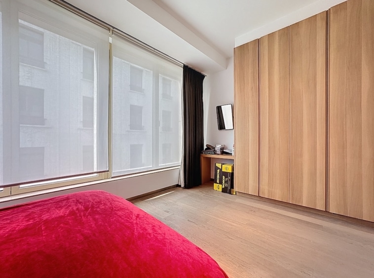 Chambre moderne et épurée avec lit rouge, grande fenêtre et mobilier en bois clair.