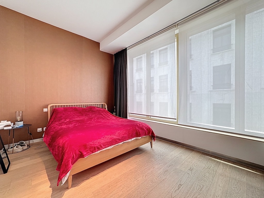 Chambre moderne chaleureuse avec lit rouge, luminosité naturelle et décoration minimaliste en bois clair.