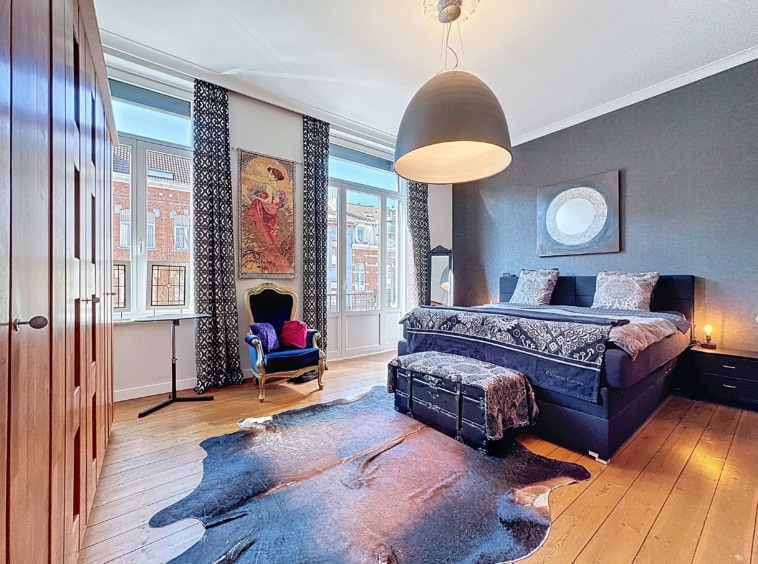 Chambre élégante avec lit raffiné, murs foncés, éclairage moderne, œuvre dart colorée et ambiance chaleureuse.