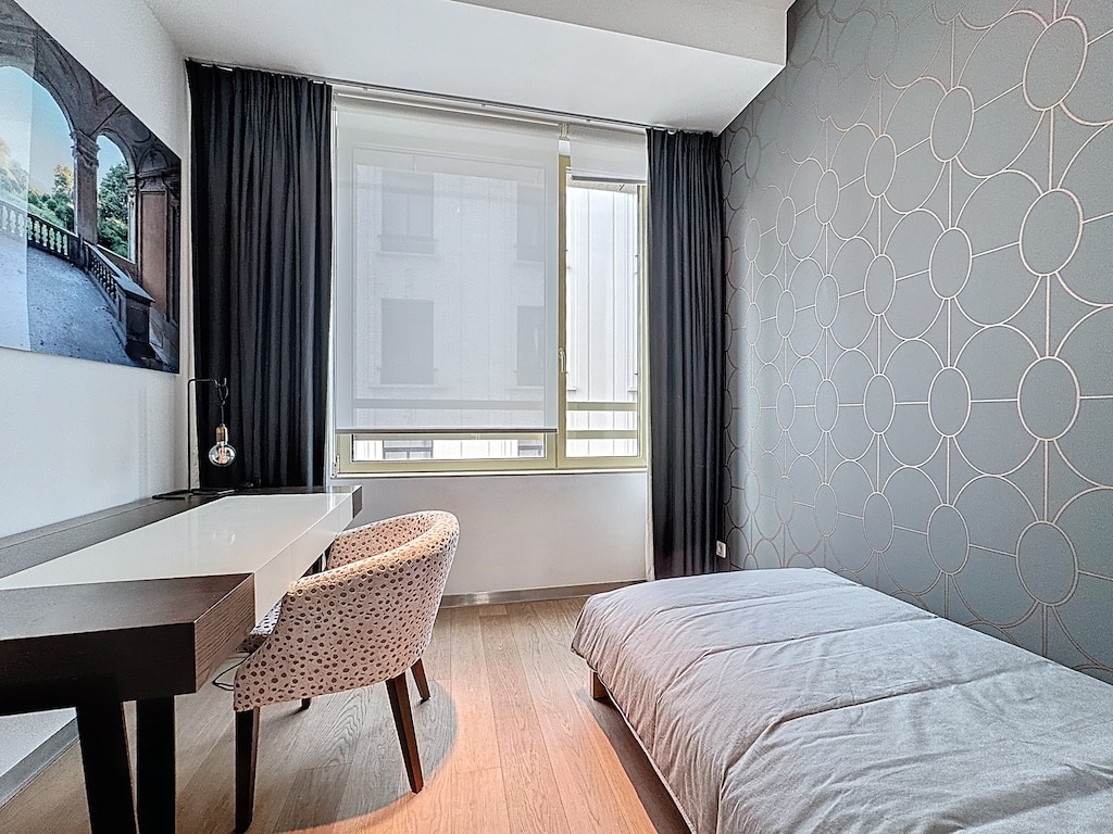 Chambre minimaliste moderne avec lit, bureau, grande fenêtre et décoration géométrique apaisante.